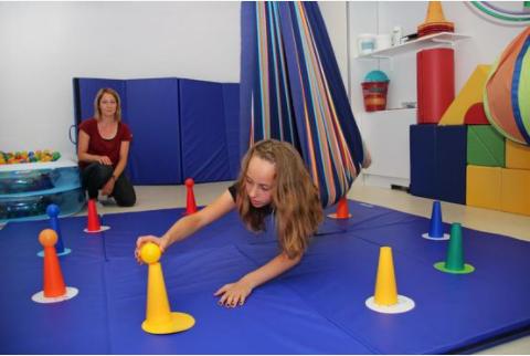 Kind in Hängetuchvorrichtung setzt einen Ball auf einen Kegel im Sportraum von Ergotherapie Hand in Hand